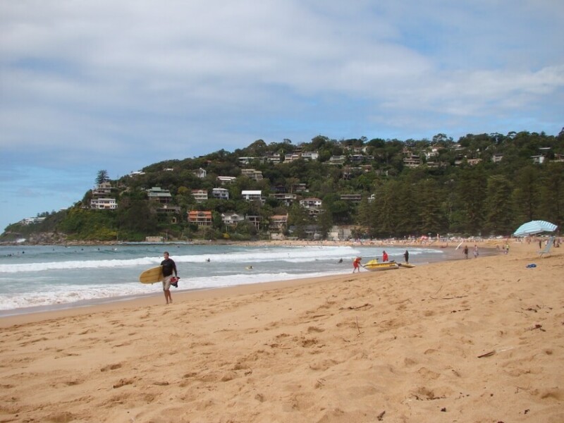 Man Walking Along the Shore with a Surfboard