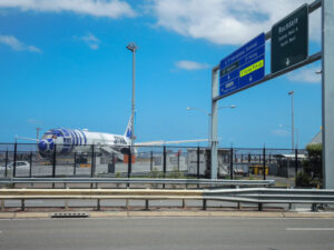 Airplane with R2-D2 livery is parked at Sydney Airport near a highway. The sky is clear, and nearby road signs point to the International Terminal.