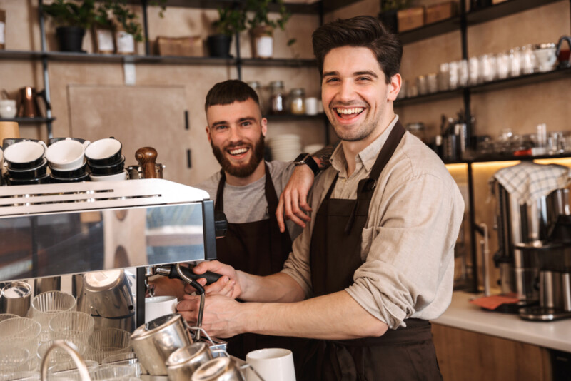 Group of cheerful men baristas wearing aprons working