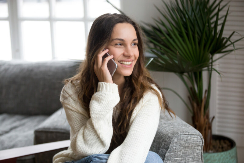 Smiling millennial woman talking on the phone at home