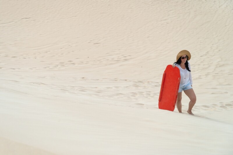 Woman climbing up a sand dune with a sandboard