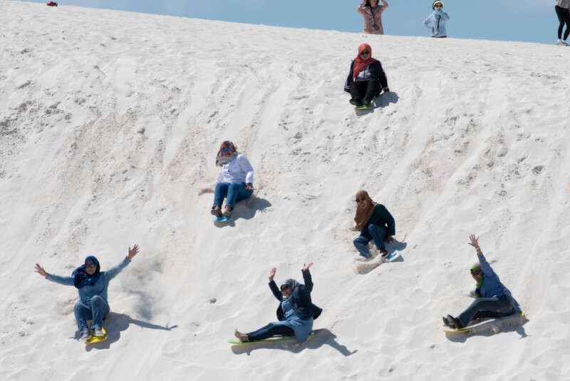 Women sandboarding down a hill