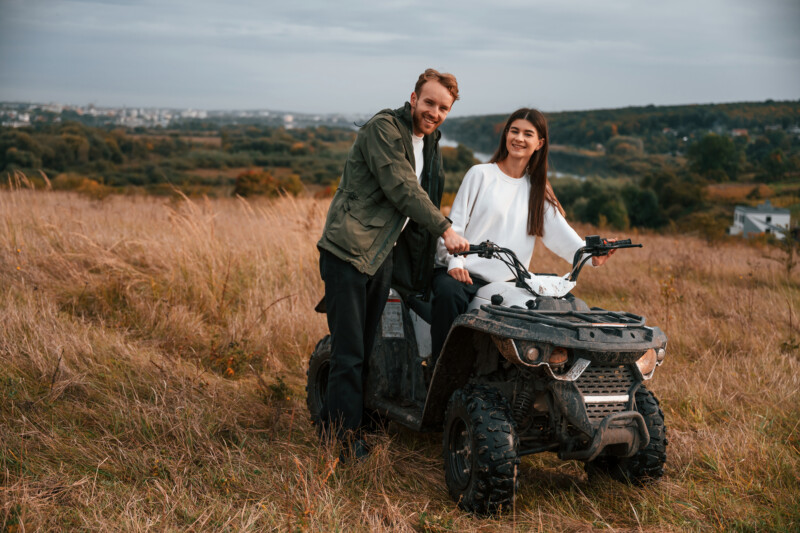 Lovely young couple is with quad bike outdoors on the field